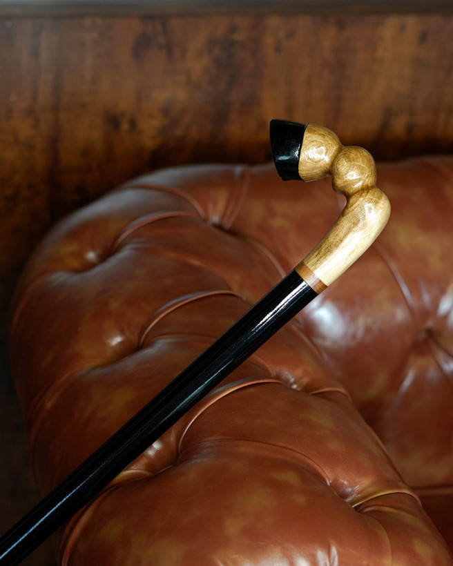 نمای نزدیک دسته پیکری عصا طرح سم اسب از چوب گردوی گیلان با رگههای طبیعی و بخشهایی رنگشده مشکی.